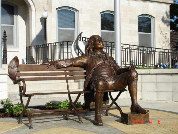 Bronze man sitting on a bench reading newspaper statue