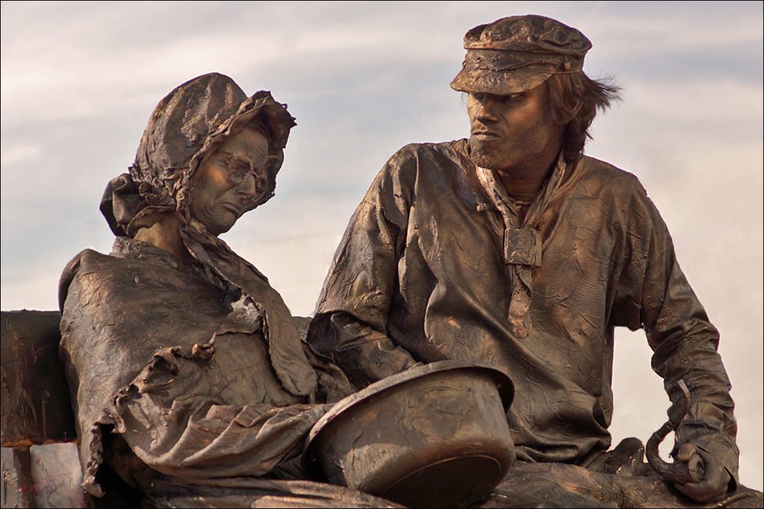 Bronze man sitting on a bench reading newspaper statue