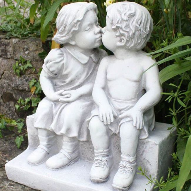 Garden statues boy and girl kissing on bench