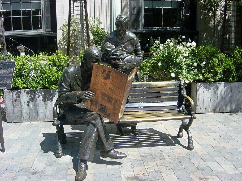 Bronze man sitting on a bench reading newspaper statue