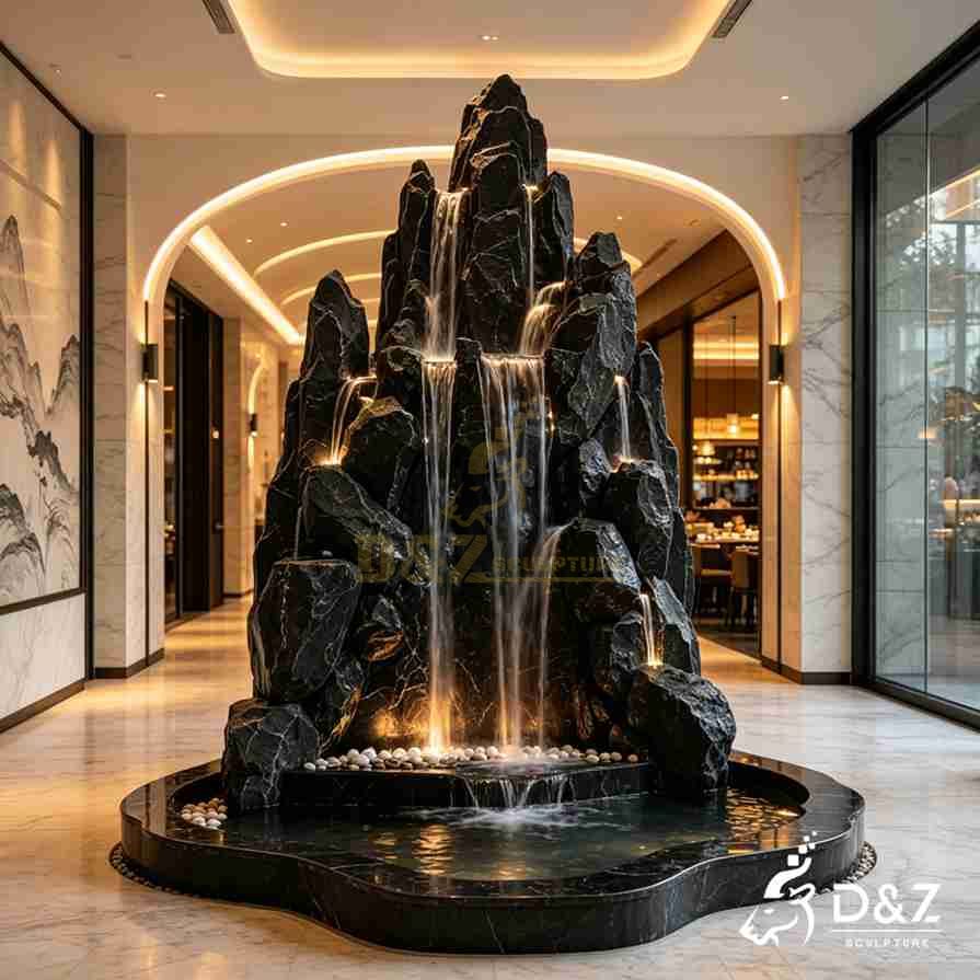 Multi-peak black marble indoor fountain with cascading streams, warm lighting, and white pebbles Multi-peak black marble indoor fountain with cascading streams, warm lighting, and white pebbles