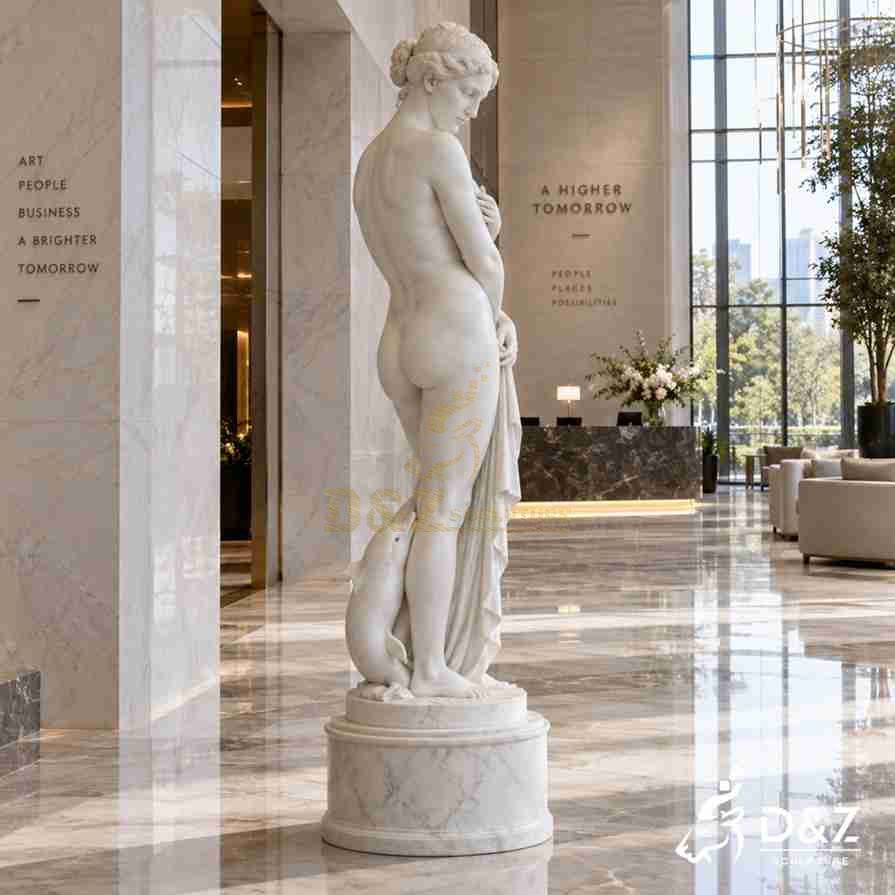 Side and rear view of a marble Venus Pudica statue with flowing drapery and dolphin detail in a modern hotel lobby