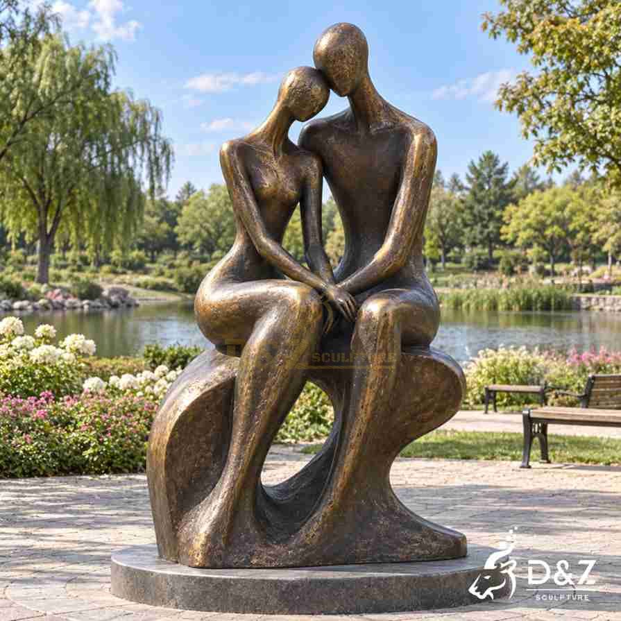 Bronze couple embracing sculpture with two abstract figures sitting closely together beside a lakeside garden Bronze couple embracing sculpture with two abstract figures sitting closely together beside a lakeside garden