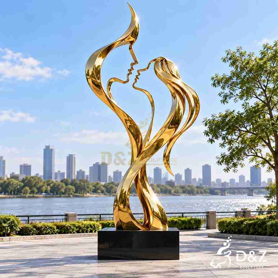 Golden abstract love sculpture of a kissing couple installed beside a waterfront landscape