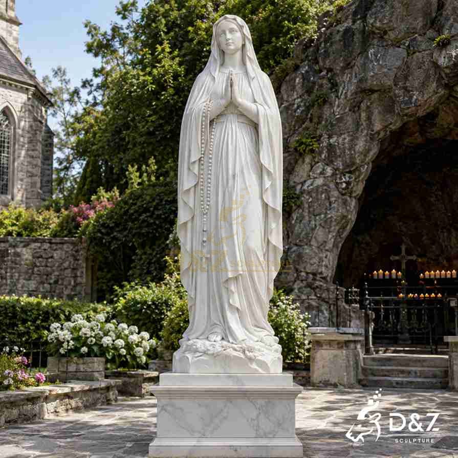 White marble Lourdes Virgin Mary statue with joined hands, a rosary, and roses at her feet beside a grotto