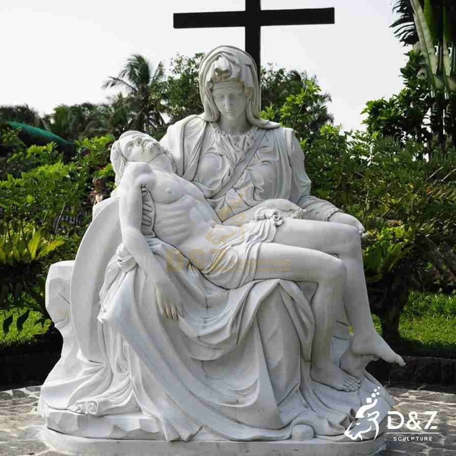 Outdoor white marble Pieta statue with Mary looking down at Jesus and a large cross behind the figures. Outdoor white marble Pieta statue with Mary looking down at Jesus and a large cross behind the figures.
