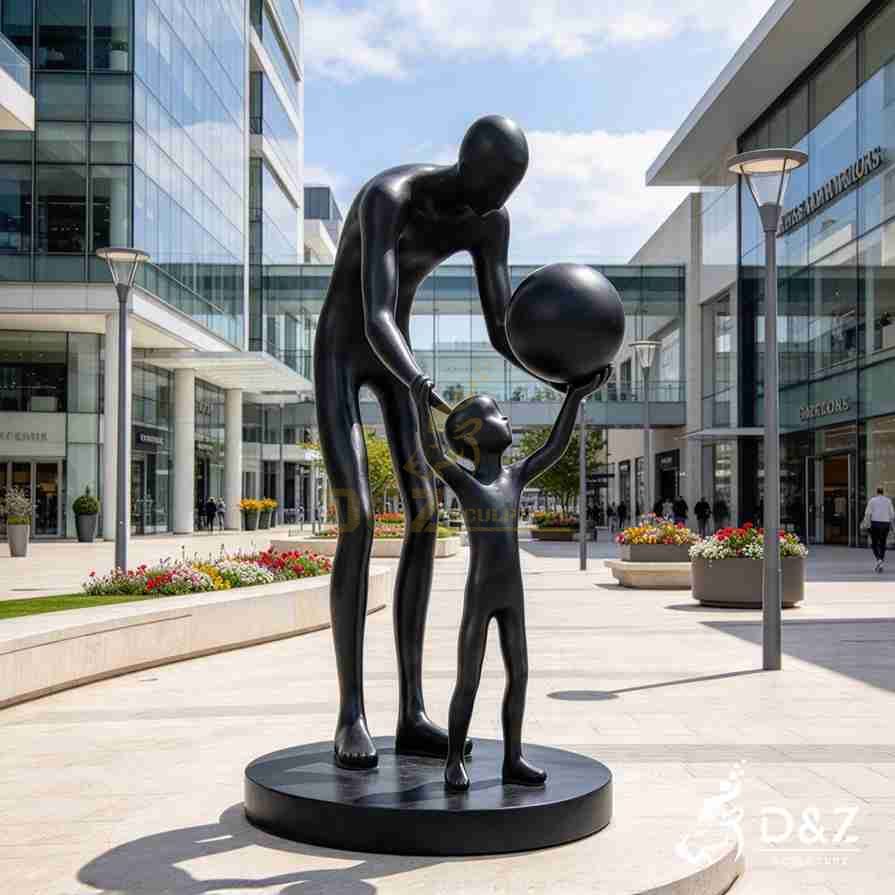 Black metal father and son sculpture showing a father holding his son's hand as the child raises a large ball. Black metal father and son sculpture showing a father holding his son's hand as the child raises a large ball.
